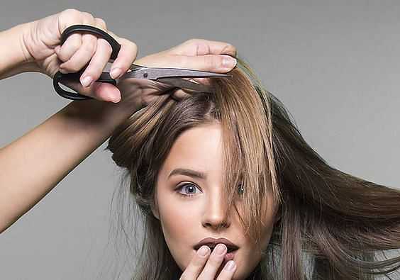 Woman getting a haircut, holding hair while stylist trims with scissors.