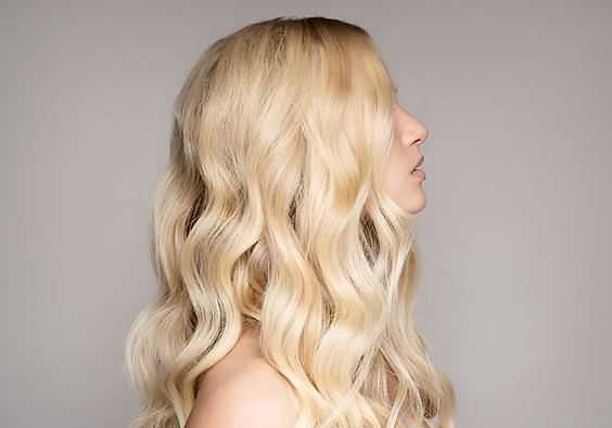 Blonde woman with long, wavy hair in profile against a neutral background.
